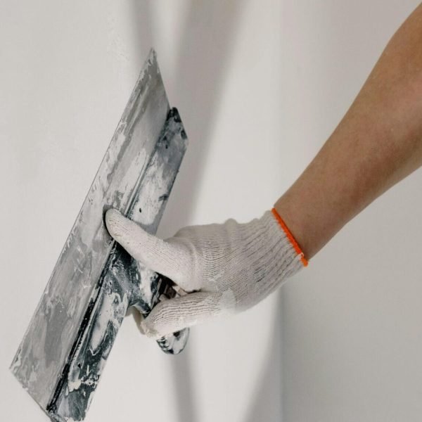 worker in gloves holding putty knife while working at home